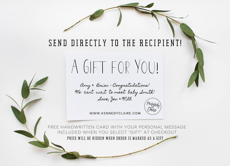 Op de afbeelding: Een witte kaart met de tekst "A Gift For You!" en een handgeschreven bericht dat luidt: "Amy & Brian - Congratulations! We can't wait to meet baby Smith! Love, Jen & Will". De kaart bevat ook het websiteadres "WWW.KENNEDYCLAIRE.COM" en een klein rond logo met de tekst "Kennedy Claire". De kaart is omringd door groene bladeren.
