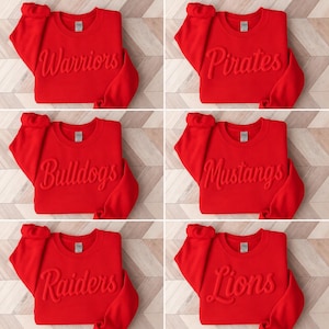 Puede incluir: Una colecci&oacute;n de seis sudaderas de cuello redondo en color rojo brillante, cada una con un nombre de equipo diferente grabado en relieve con letra cursiva en el pecho. Los nombres son Warriors, Pirates, Bulldogs, Mustangs, Raiders y Lions. Cada prenda tiene mangas largas y cuello acanalado.