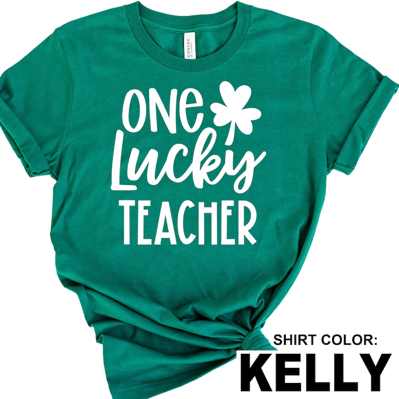 May include: A Kelly green t-shirt with the text "ONE Lucky TEACHER" in white, along with a white shamrock. The shirt is made of a soft material and has rolled-up sleeves.