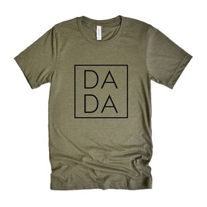 Puede incluir: Una camiseta verde con la palabra "DA DA" impresa en un cuadrado negro en la parte delantera.