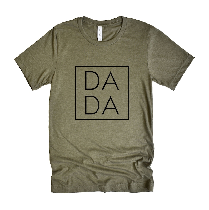Puede incluir: Una camiseta verde con la palabra "DA DA" impresa en un cuadrado negro en la parte delantera.
