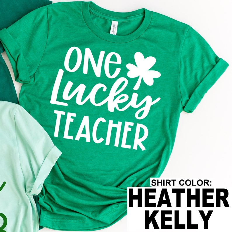 May include: A green t-shirt with the text "ONE Lucky TEACHER" in white, along with a white shamrock. The shirt is a Heather Kelly color.