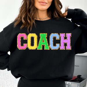May include: Black sweatshirt with the word "COACH" in colorful glitter letters.