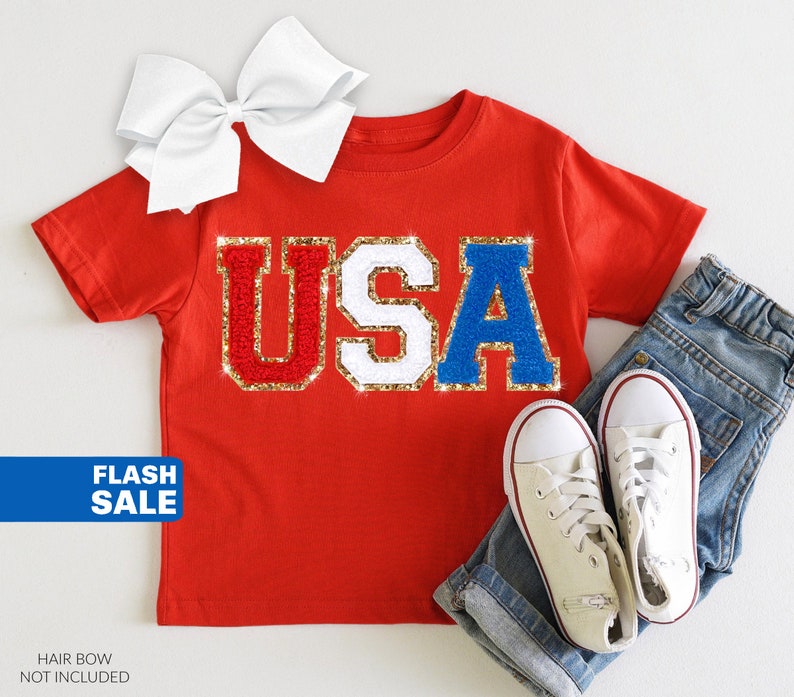 May include: Red, white, and blue glitter "USA" graphic on a red t-shirt.