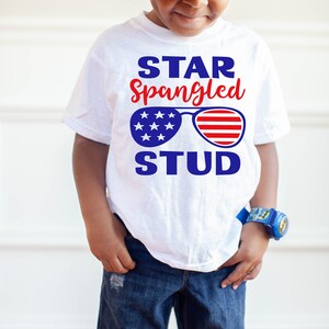 May include: A white t-shirt with a blue and red graphic of sunglasses with stars and stripes. The text "STAR Spangled STUD" is printed on the shirt.