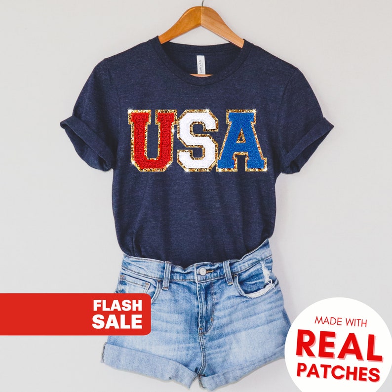 May include: Navy blue t-shirt with the word "USA" in red, white, and blue sequined patches. The shirt is paired with denim shorts. The image also includes the text "FLASH SALE" and "MADE WITH REAL PATCHES".