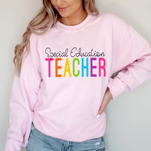 May include: Pink sweatshirt with the text "Special Education TEACHER" in rainbow colors.