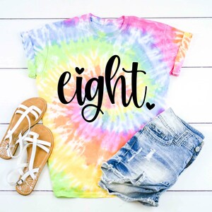 May include: A tie-dye t-shirt with the word "eight" written in black cursive with a small heart above the "e" and a small heart after the "t".