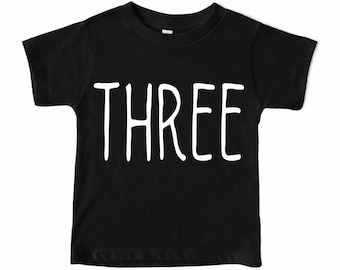 May include: Black short-sleeved t-shirt with the word "THREE" written in white.