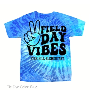 Puede incluir: Camiseta azul te&ntilde;ida con la frase "FIELD DAY VIBES" en negro y un signo de la paz. El texto "STAR HILL ELEMENTARY" est&aacute; debajo. La camiseta tiene cuello redondo.