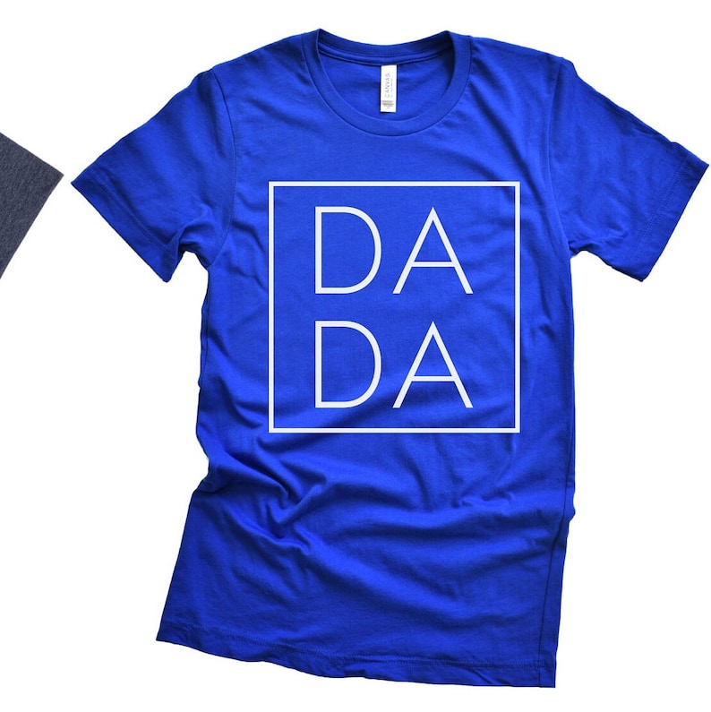 Puede incluir: Una camiseta azul real con un cuadrado blanco que contiene el texto "DA DA" en una fuente en negrita sin serif.