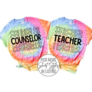 May include: Two tie-dye t-shirts with the words "COUNSELOR" and "TEACHER" printed in black on a rainbow background.