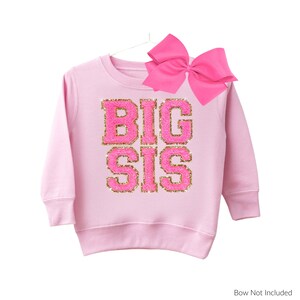 May include: Pink sweatshirt with the words "BIG SIS" in gold glitter letters on a pink background.
