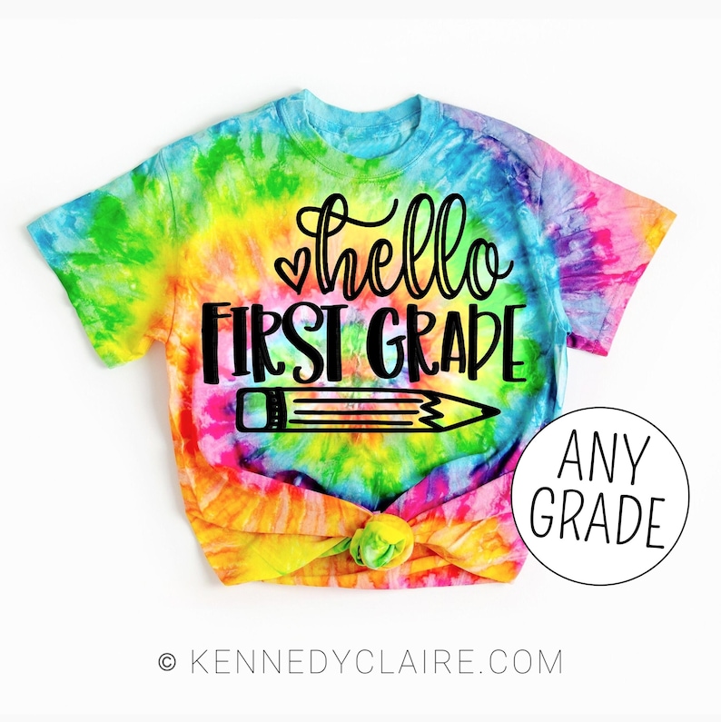 May include: A tie-dye t-shirt with the text "hello first grade" and a pencil graphic. The text "any grade" is also visible in the image.