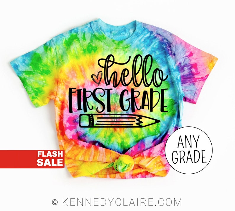 May include: A tie-dye t-shirt with the text "hello first grade" and a pencil graphic. The shirt is available in any grade.