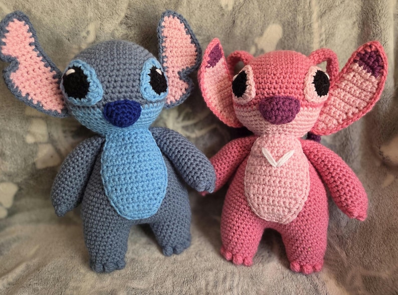 May include: Two crocheted plush toys, one blue and one pink, resembling the characters Stitch and Angel from the Disney movie Lilo & Stitch.