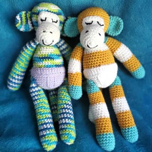 May include: Two handmade crochet monkey dolls. One monkey has blue, green, and white striped arms and legs, a purple belly, and a striped head. The other monkey has yellow, white, and blue striped arms and legs and a yellow head.