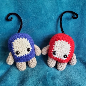 May include: Two crocheted plush toys with black yarn antennae. One is blue with white eyes and a white face, the other is red with white eyes and a white face.