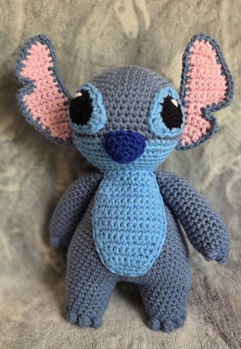 May include: A blue and pink crocheted Stitch plush toy with black eyes and a blue nose.