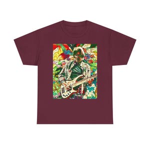 May include: Burgundy t-shirt featuring a colorful graphic of a musician playing a bass guitar. The graphic has a stained-glass effect with floral and abstract elements. The musician is wearing a plaid shirt and sunglasses.