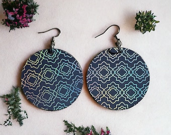 May include: Circular, dark blue earrings featuring an iridescent geometric design. The earrings have a hook fastening and are presented on a pale surface. These earrings are a fashion accessory.