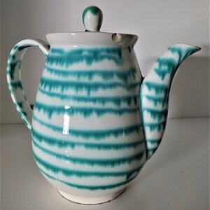 Pu&ograve; includere: Una teiera in ceramica bianca con un motivo a strisce verdi e bianche. La teiera ha un coperchio e un beccuccio.