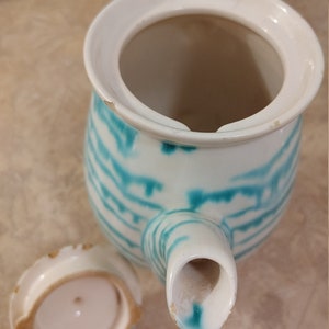 Pu&ograve; includere: Una teiera bianca con un design a strisce verde acqua e bianco. La teiera ha un coperchio e un beccuccio. Il coperchio &egrave; rimosso e si trova accanto alla teiera.