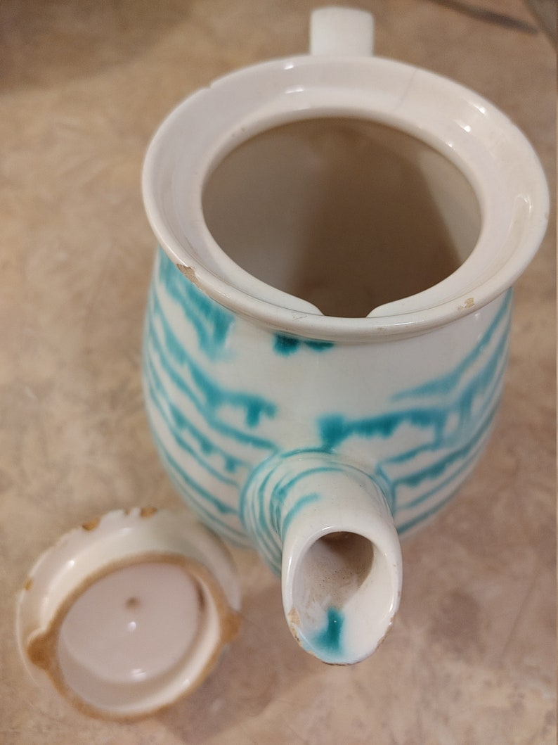 Pu&ograve; includere: Una teiera bianca con un design a strisce verde acqua e bianco. La teiera ha un coperchio e un beccuccio. Il coperchio &egrave; rimosso e si trova accanto alla teiera.