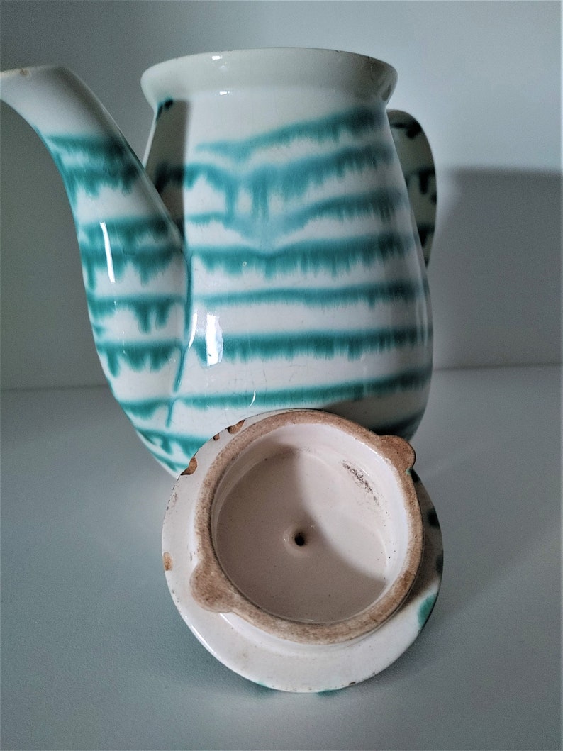 Pu&ograve; includere: Una teiera in ceramica bianca con un motivo a strisce verdi e bianche. La teiera ha un coperchio che &egrave; stato tolto e si trova accanto alla teiera.