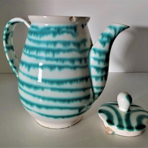 Pu&ograve; includere: Una teiera in ceramica bianca con un design a strisce verdi e bianche. La teiera ha un coperchio e un manico.