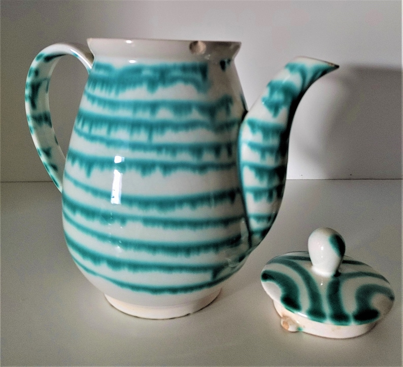 Pu&ograve; includere: Una teiera in ceramica bianca con un design a strisce verdi e bianche. La teiera ha un coperchio e un manico.