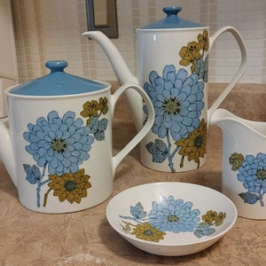 May include: A white ceramic tea set with a blue and yellow floral pattern. The set includes a teapot, creamer, sugar bowl, and a saucer.