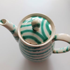 May include: A white teapot with a green and white striped design. The lid has a green and white swirl pattern.