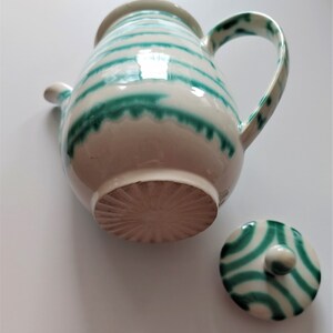 Pu&ograve; includere: Una teiera in ceramica bianca con strisce verdi e un coperchio abbinato. La teiera ha un corpo arrotondato e un manico sul lato. Il coperchio ha un pomo in cima.