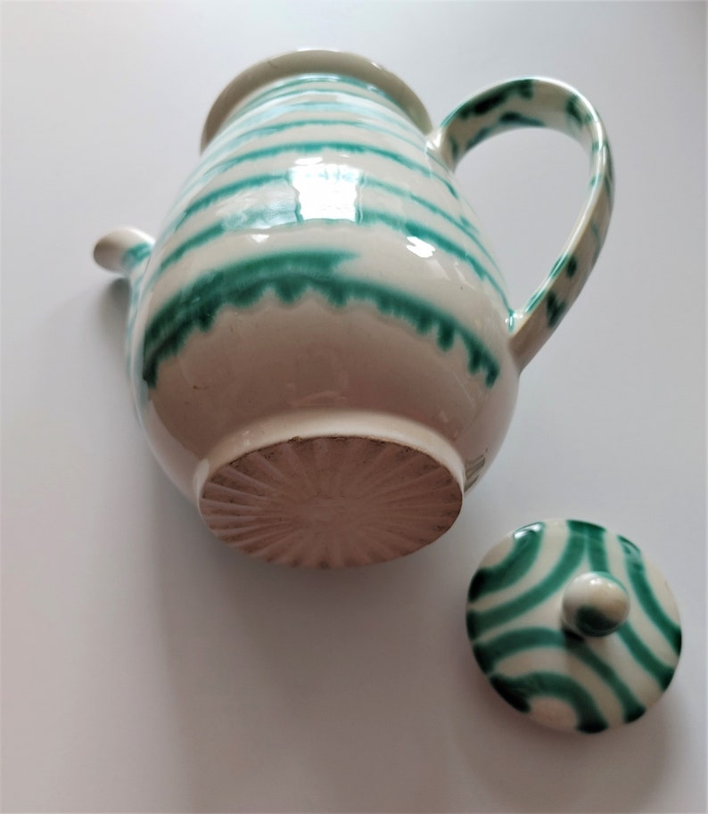 Pu&ograve; includere: Una teiera in ceramica bianca con strisce verdi e un coperchio abbinato. La teiera ha un corpo arrotondato e un manico sul lato. Il coperchio ha un pomo in cima.