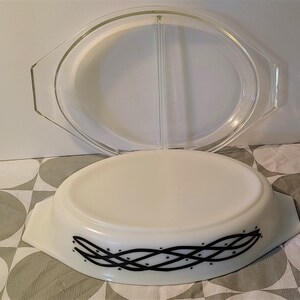 May include: An oval, white Pyrex baking dish with a clear glass lid. The dish has a black, woven design with small star accents. The lid is divided into two sections. The dish is designed for baking and serving.