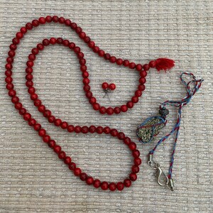 May include: A red beaded necklace with a tassel, a pair of red bead earrings, and a small, gold-colored pendant on a blue and red cord.