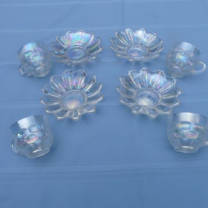 Peut inclure: Ensemble de six tasses à thé et soucoupes en verre iridescent. Les tasses et les soucoupes ont un design en forme de fleur et sont transparentes avec une finition irisée.