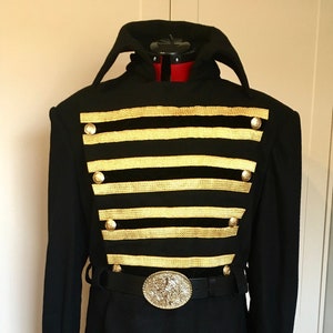 May include: A black long-sleeved coat with gold trim and buttons. The coat has a high collar and a belt with a large, ornate buckle.