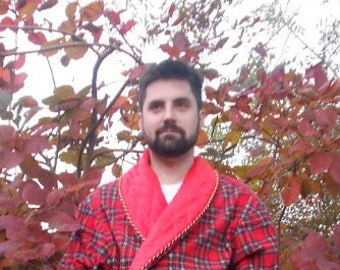 May include: A man wearing a red and black plaid robe with a red velvet collar. The robe has a gold trim around the collar and pockets.