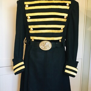 May include: A black long coat with a high collar and gold trim. The coat has a belt with a large, ornate buckle. The coat is on a mannequin.