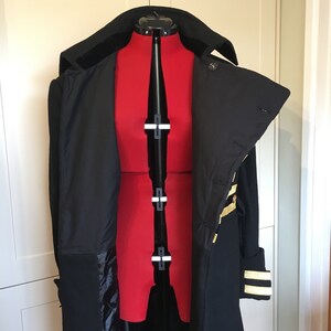 May include: A black double-breasted coat with gold trim on the sleeves and collar. The coat is open and the lining is visible.