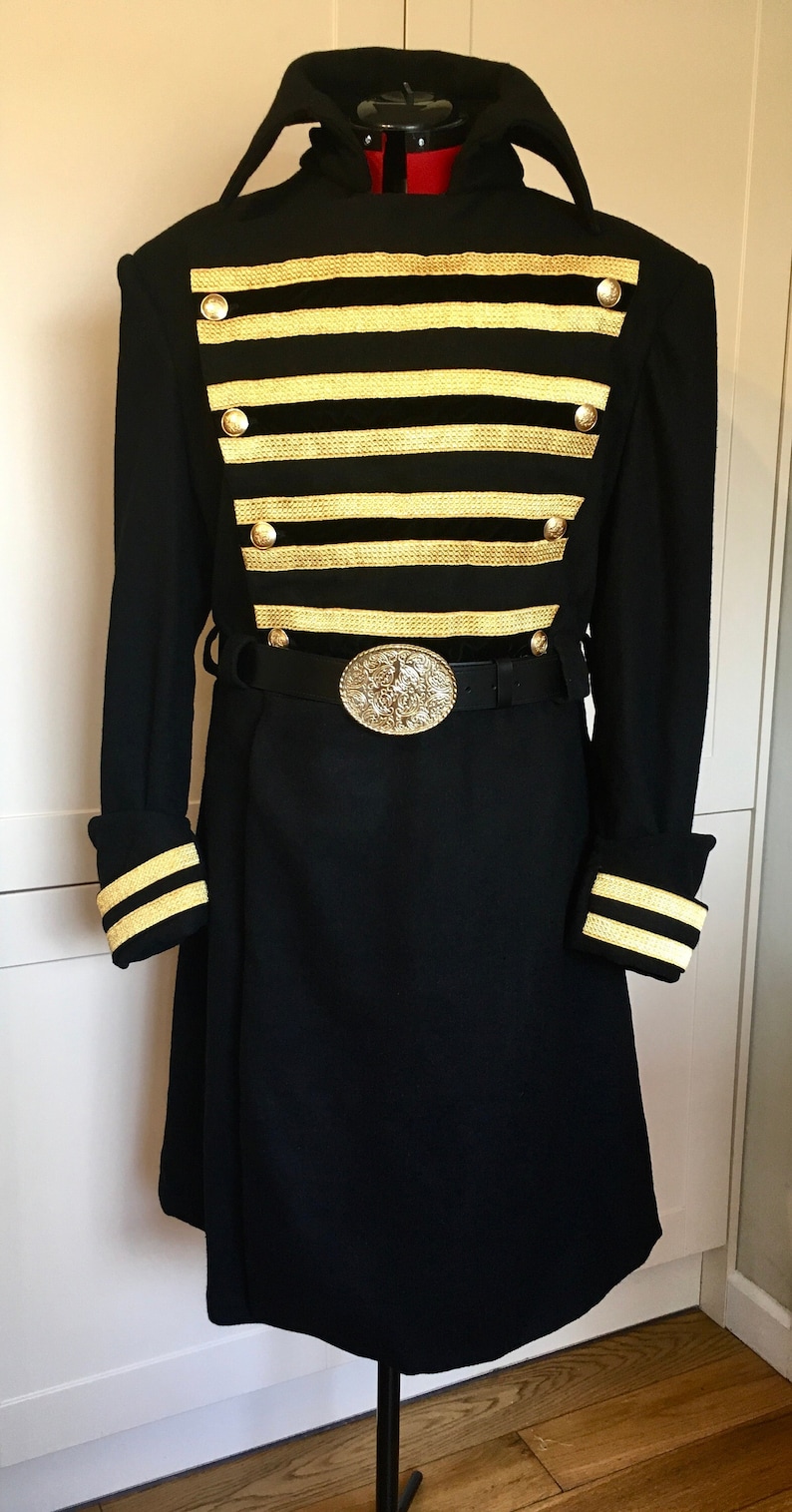 May include: A black long-sleeved coat with gold trim and buttons. The coat has a high collar and a belt with a large, ornate buckle.