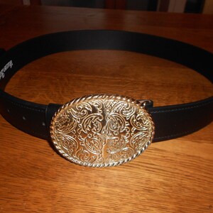 May include: A black leather belt with a large, ornate gold-toned buckle. The buckle features a paisley-like design.