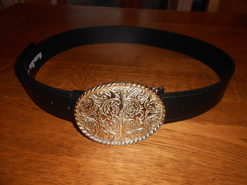 May include: A black leather belt with a large, ornate gold-toned buckle. The buckle features a paisley-like design.