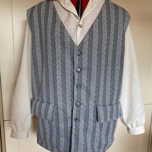 Op de afbeelding: Een driedelig ensemble met een crèmekleurig overhemd met kraag, een blauw-wit gestreept vest met vier knopen en een bijpassende gestreepte jas. Het vest heeft twee zakken.
