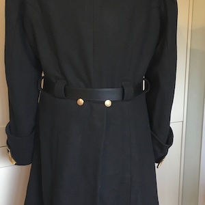 May include: A black wool coat with a black leather belt and gold buttons. The coat has a collar and long sleeves.