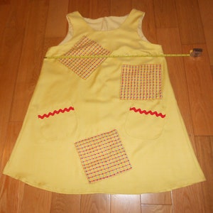 May include: A yellow sleeveless dress with red and white checkered fabric patches and red zig-zag trim on the pockets.
