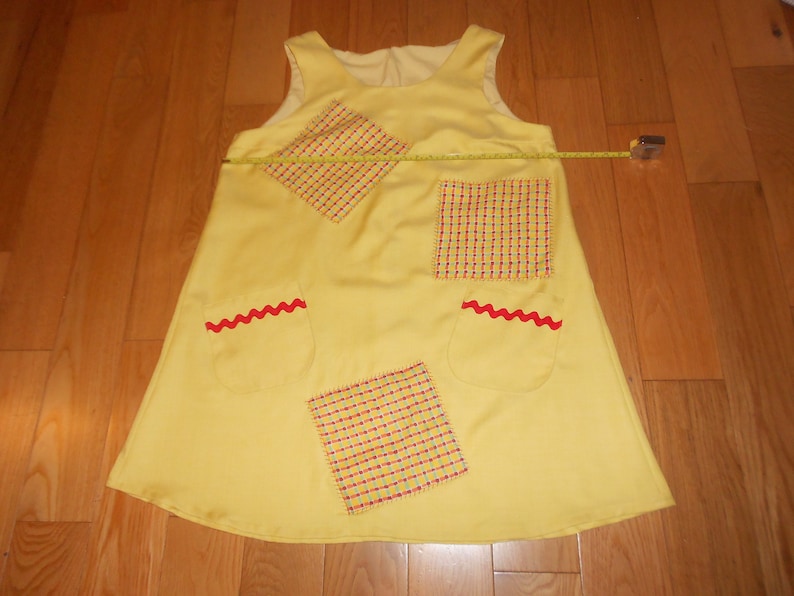 May include: A yellow sleeveless dress with red and white checkered fabric patches and red zig-zag trim on the pockets.