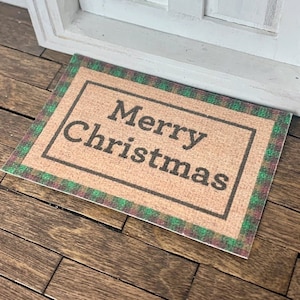 May include: A brown doormat with a green and red plaid border. The doormat has the text "Merry Christmas" in black lettering.
